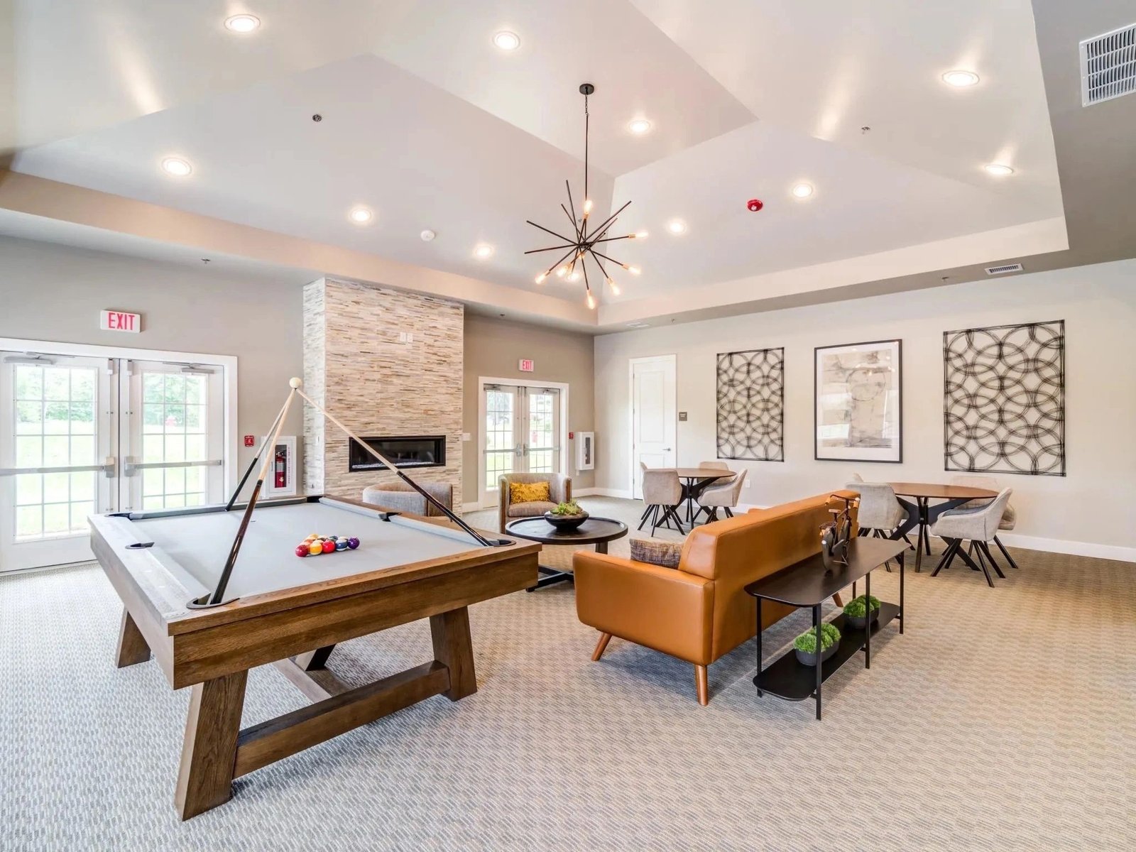 A bright residential-community resident lounge with billiards, a stone fireplace and lounge seating, styled by Cameo Group